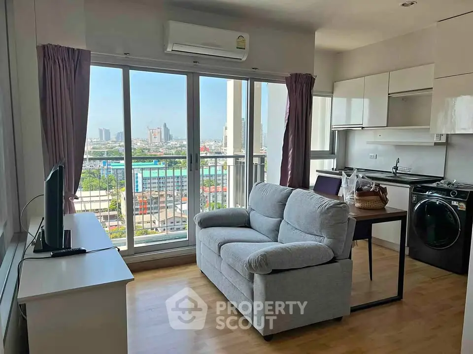 Modern living room with city view, featuring cozy sofa, TV, and compact kitchen with washing machine.