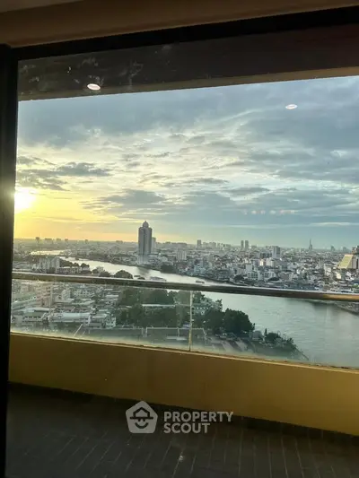 Stunning high-rise view of city skyline and river at sunset from a balcony.