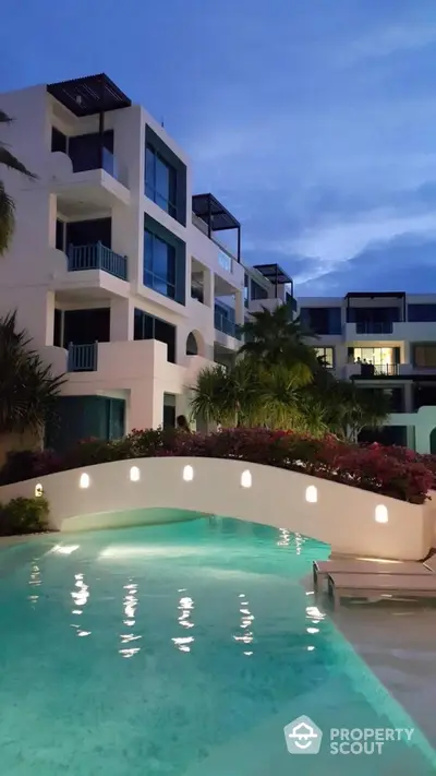 Luxurious modern apartment complex with stunning pool and lush landscaping at dusk.