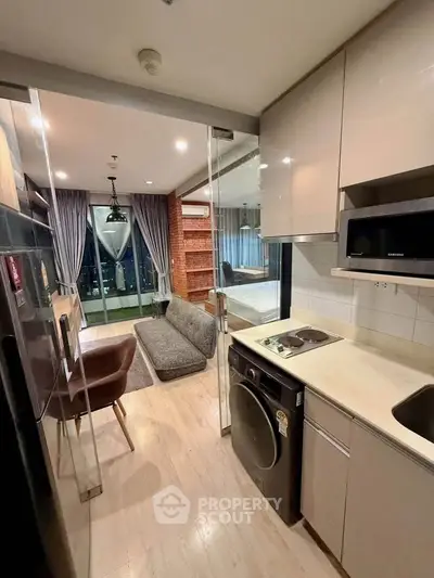 Modern apartment interior with open kitchen and cozy living area, featuring a washing machine and city view.