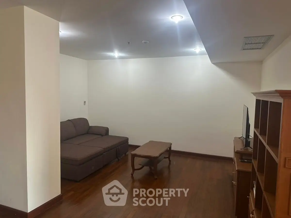 Cozy living room with wooden flooring and modern lighting, featuring a comfortable sofa and TV setup.
