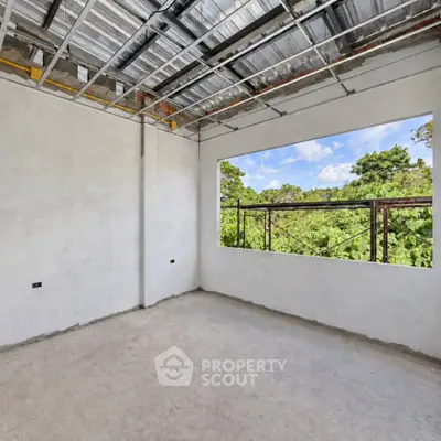 Spacious unfinished room with large window offering lush greenery view, perfect for customization.