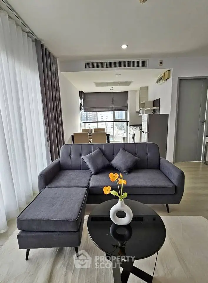 Modern living room with sleek furniture and open kitchen layout in a high-rise apartment.
