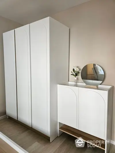 Modern bedroom with sleek white wardrobe and stylish cabinet with mirror.