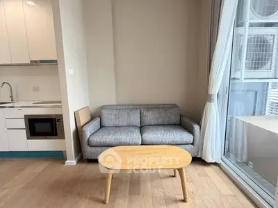 Modern living room with cozy sofa and kitchenette, featuring large window for natural light.
