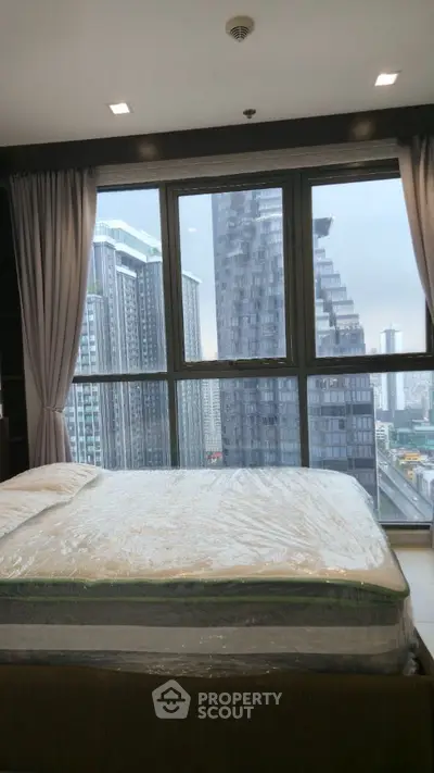 Modern bedroom with city view from large window, featuring a neatly made bed.