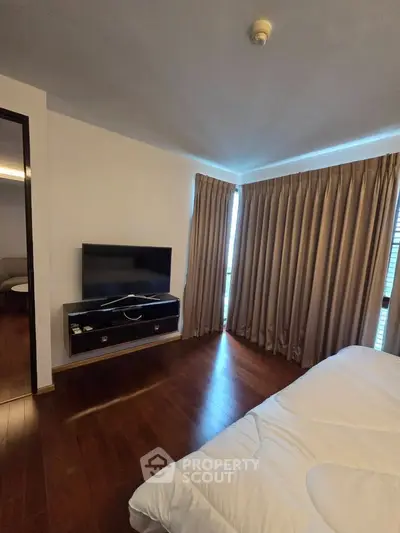 Spacious bedroom with wooden flooring and large windows for natural light
