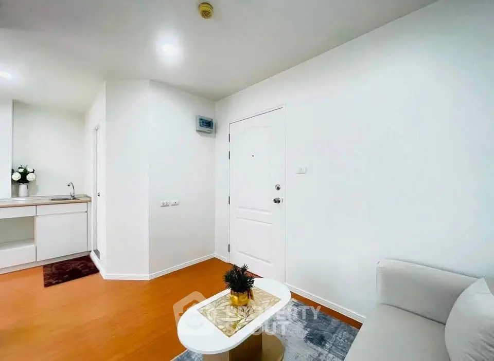 Modern minimalist living room with white walls, cozy sofa, and small kitchenette.