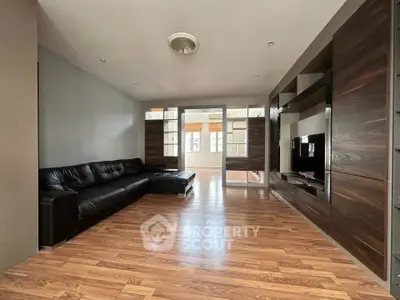 Spacious modern living room with sleek wooden flooring and stylish black leather sofa.