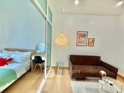 Modern studio apartment with cozy living area and stylish bedroom separated by glass partition.