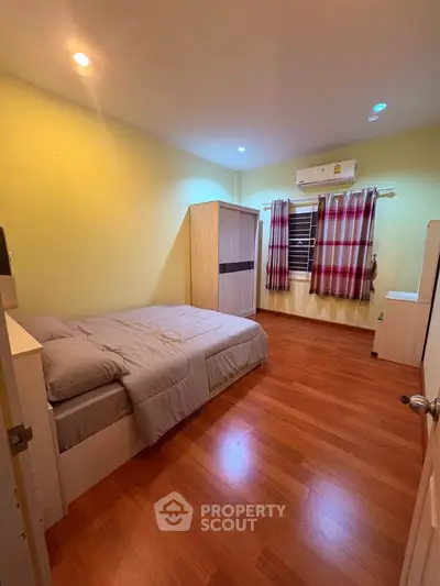 Cozy bedroom with wooden flooring and air conditioning, featuring a comfortable bed and stylish curtains.