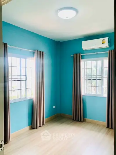 Bright bedroom with blue walls and large windows, featuring air conditioning.