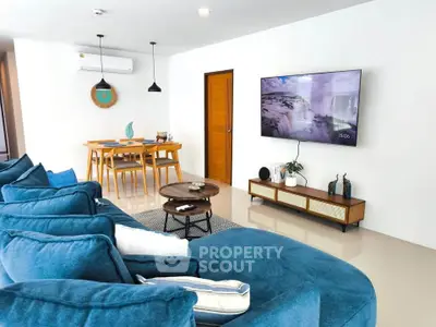 Modern living room with blue sofa, wall-mounted TV, and dining area in open layout.