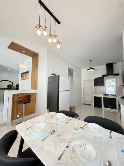 Modern kitchen with dining area, featuring sleek appliances and stylish lighting.