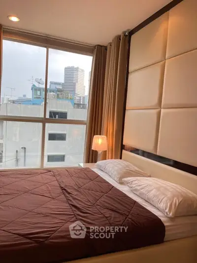 Modern bedroom with large window offering city view, featuring elegant decor and cozy ambiance.