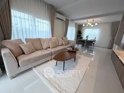 Elegant living room with plush sofa and modern dining area, featuring large windows and stylish lighting.