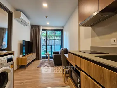 Modern open-layout living room with kitchen, featuring sleek furniture and natural light.