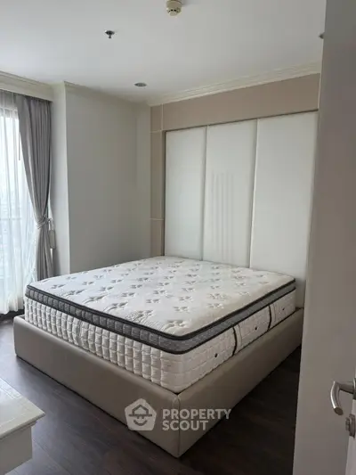 Spacious bedroom with large window and modern design in a high-rise apartment.