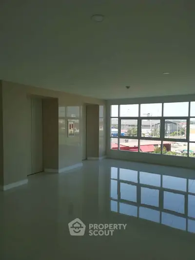 Spacious empty room with large windows offering natural light and city view.