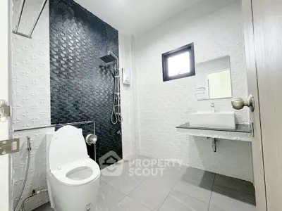 Modern bathroom with sleek black and white tiles, featuring a shower and contemporary fixtures.