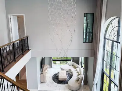 Luxurious living room with high ceilings, elegant chandelier, and large windows offering natural light.