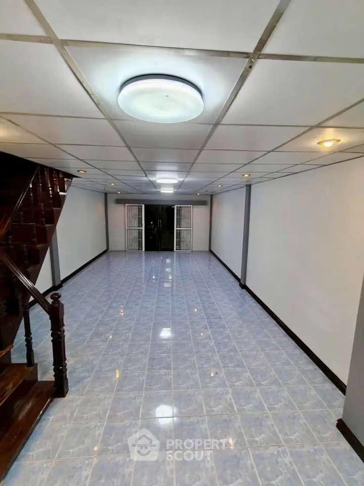Spacious tiled living room with modern ceiling lights and wooden staircase, perfect for family gatherings.