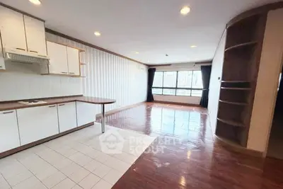Spacious open-plan living room with kitchen, featuring wooden floors and ample natural light.