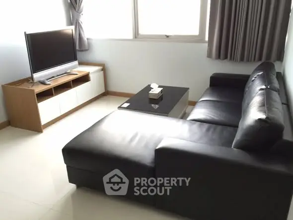 Modern living room with sleek black leather sofa and flat-screen TV, perfect for relaxation.