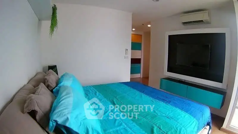 Modern bedroom with vibrant blue bedding and wall-mounted TV, featuring air conditioning.