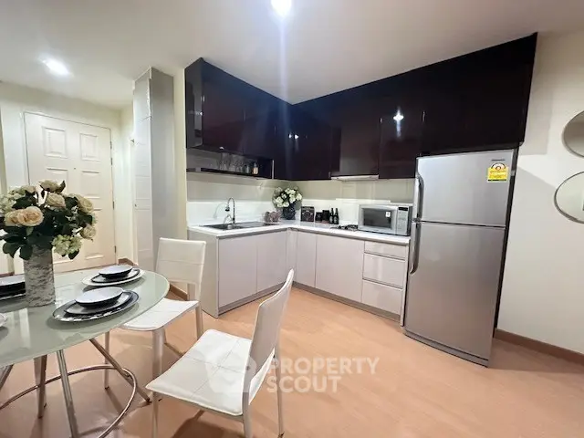Modern kitchen with sleek cabinets, dining area, and stainless steel appliances in a cozy apartment.