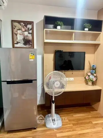 Modern living room with fridge, TV, and fan on wooden flooring.