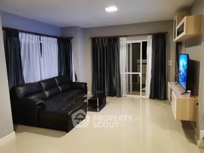 Spacious modern living room with sleek black leather sofa and large windows for natural light.