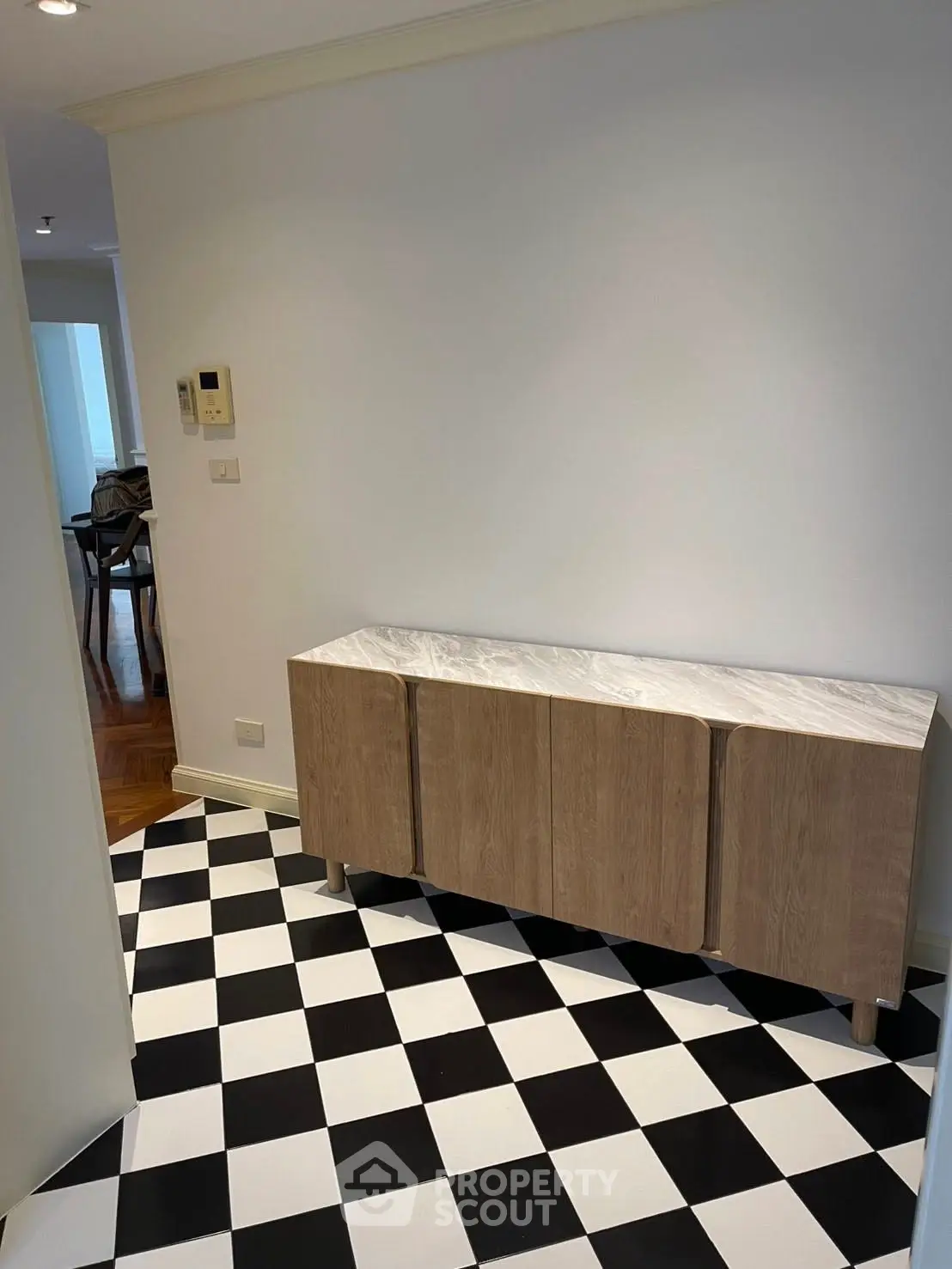 Stylish hallway with checkered floor and modern wooden cabinet, leading to a dining area.