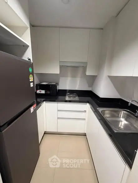 Modern compact kitchen with sleek white cabinets and black countertops, featuring a fridge and microwave.
