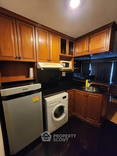 Charming kitchen with wooden cabinets, washing machine, and compact fridge in cozy apartment.