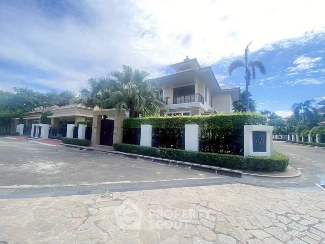 Luxurious modern villa with lush greenery and spacious driveway under a clear blue sky.