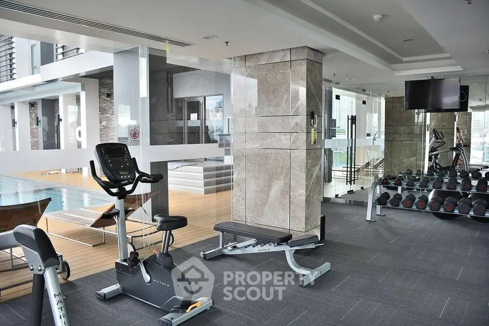 Luxurious gym with modern equipment and pool view in upscale residential building.