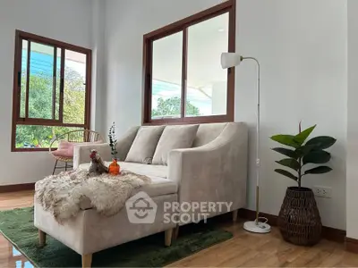 Cozy living room with plush sofa and large windows offering lush garden views.