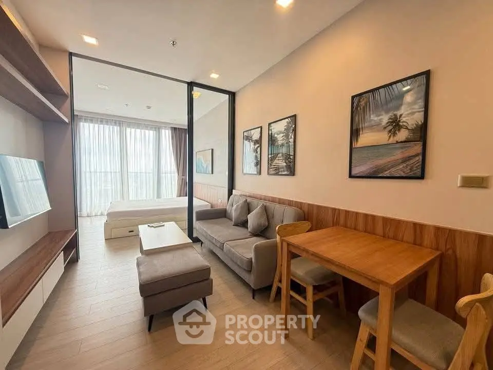 Modern living room with cozy seating and stylish decor, adjacent to a bright bedroom with large windows.