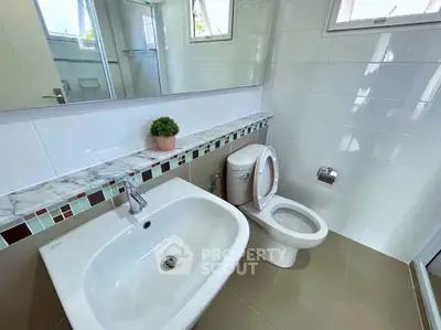 Modern bathroom with sleek sink and toilet, featuring stylish tile accents and natural light.
