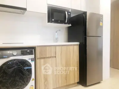 Modern kitchen with sleek appliances including fridge, microwave, and washing machine in stylish wood cabinetry.