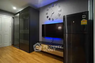 Modern living room with sleek black furniture and stylish wall clock, featuring a large TV and refrigerator.