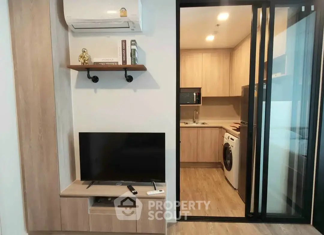 Modern apartment interior with open kitchen and living area featuring TV and washing machine.