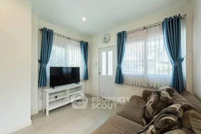 Cozy living room with natural light, blue curtains, and modern TV setup.