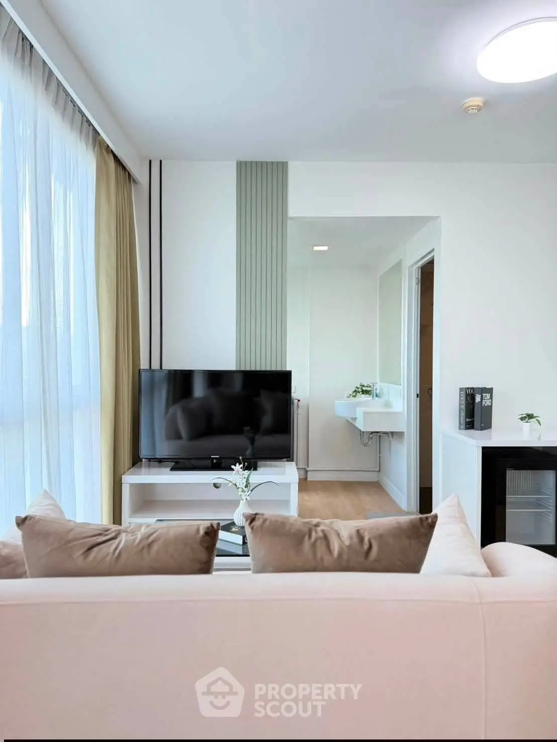 Modern living room with sleek TV setup and elegant decor, featuring a cozy sofa and natural light from large windows.