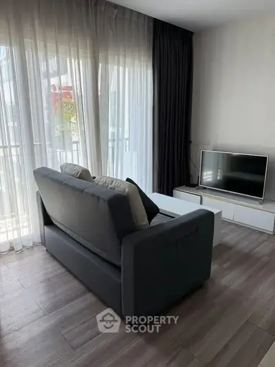 Modern living room with sleek sofa and flat-screen TV, featuring floor-to-ceiling windows and elegant curtains.