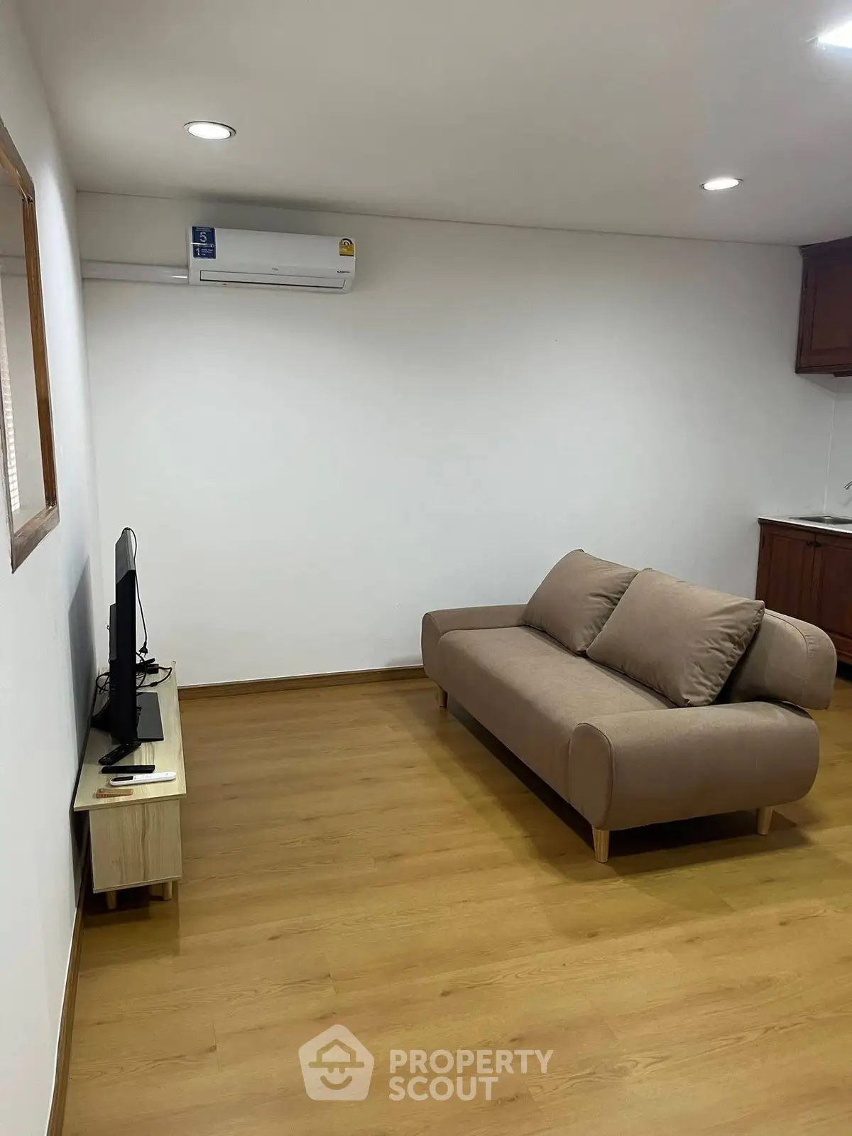 Modern living room with sleek sofa and wall-mounted TV, featuring minimalist design and wooden flooring.