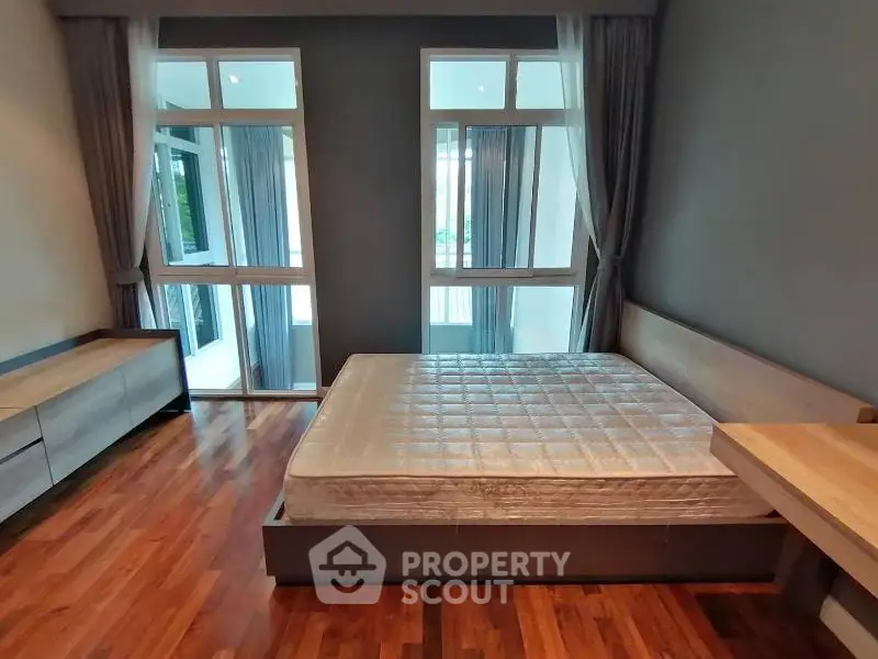 Spacious bedroom with large windows and hardwood floors in modern apartment.