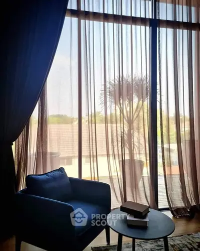 Cozy living room with large window and elegant curtains, featuring a stylish armchair and coffee table.