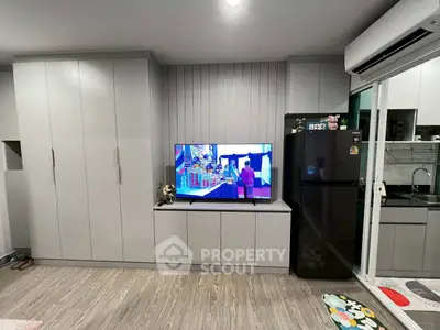 Modern living room with sleek cabinetry and TV, adjacent to a compact kitchen.